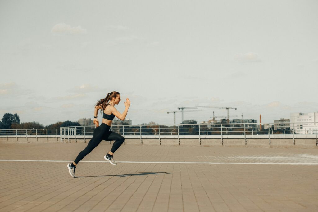 Woman sprinting on a rooftop in athletic wear during the day.